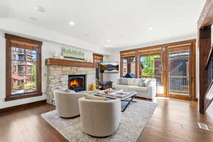 Living area featuring a stone fireplace with a wood mantle, wood-finish flooring, recessed lighting, and multiple windows with wood trim