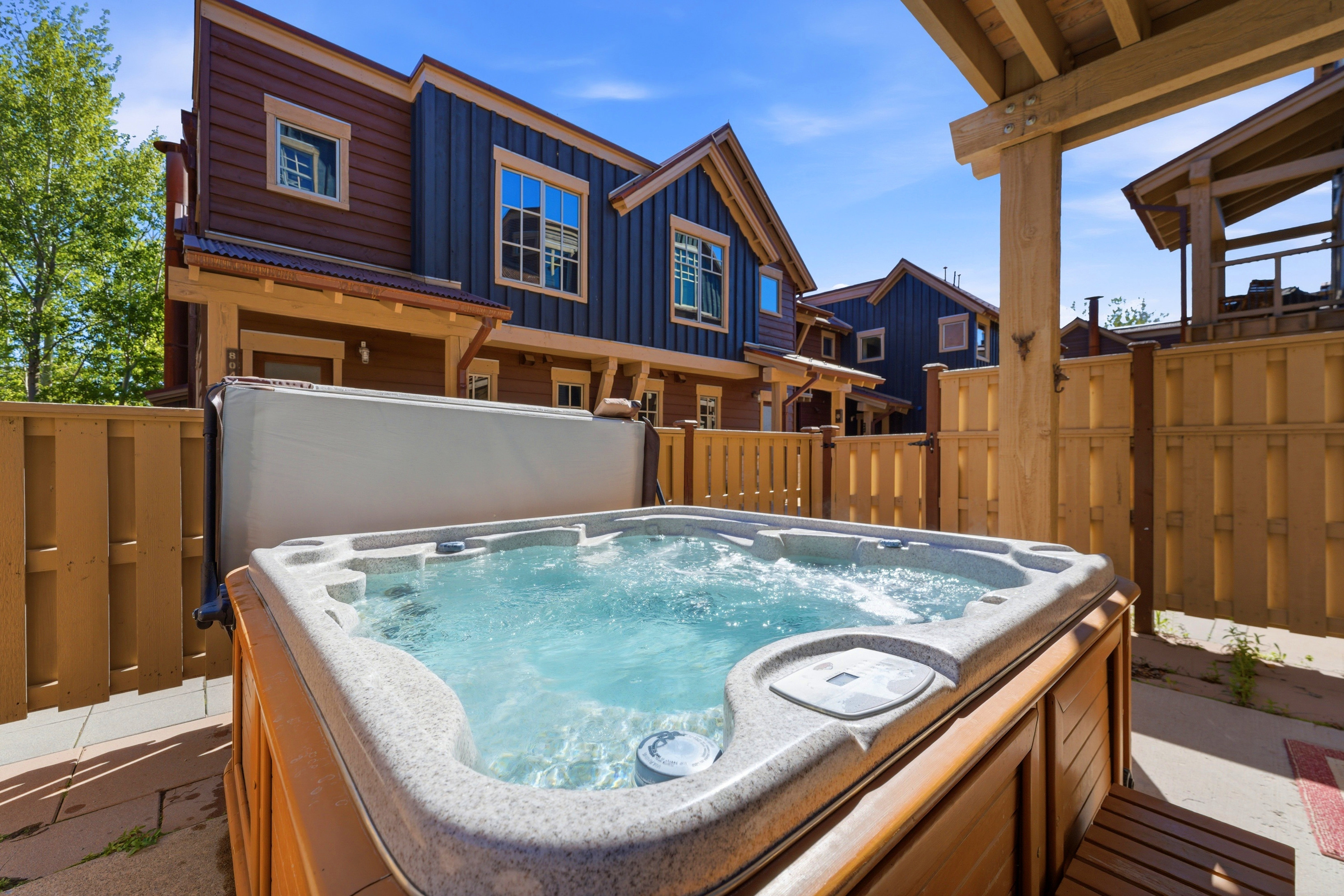 Outdoor hot tub with wooden surround, privacy fencing, and stone paver patio