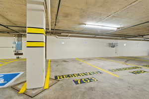 Reserved parking spaces within a concrete subterranean garage, featuring overhead fluorescent lighting, exposed utility conduits, and painted yellow line markings