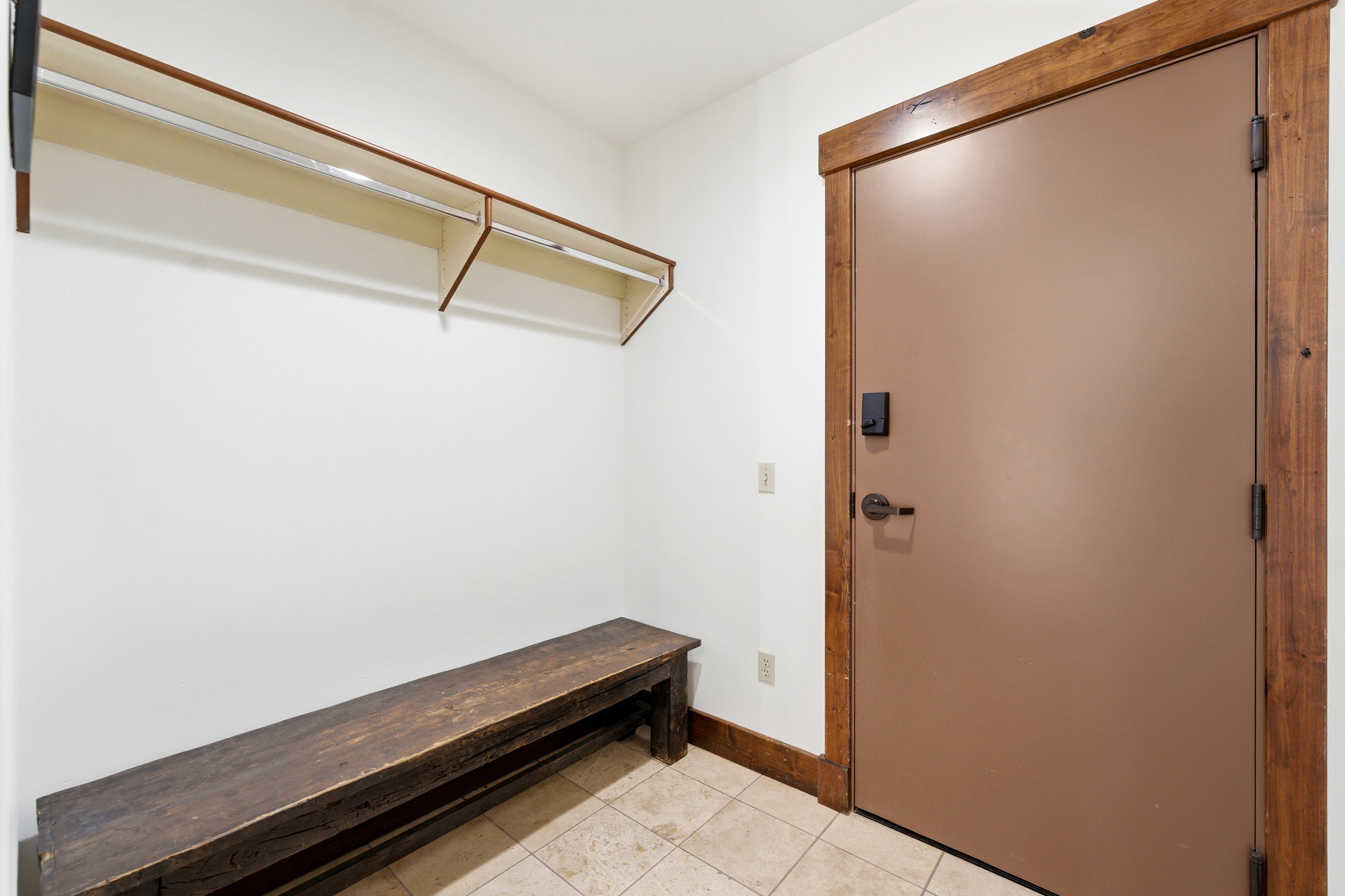 Entryway mudroom featuring a built-in wooden bench, overhead shelving with hanging rods, tile flooring, and a solid core door with wood trim