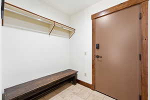 Entryway mudroom featuring a built-in wooden bench, overhead shelving with hanging rods, tile flooring, and a solid core door with wood trim