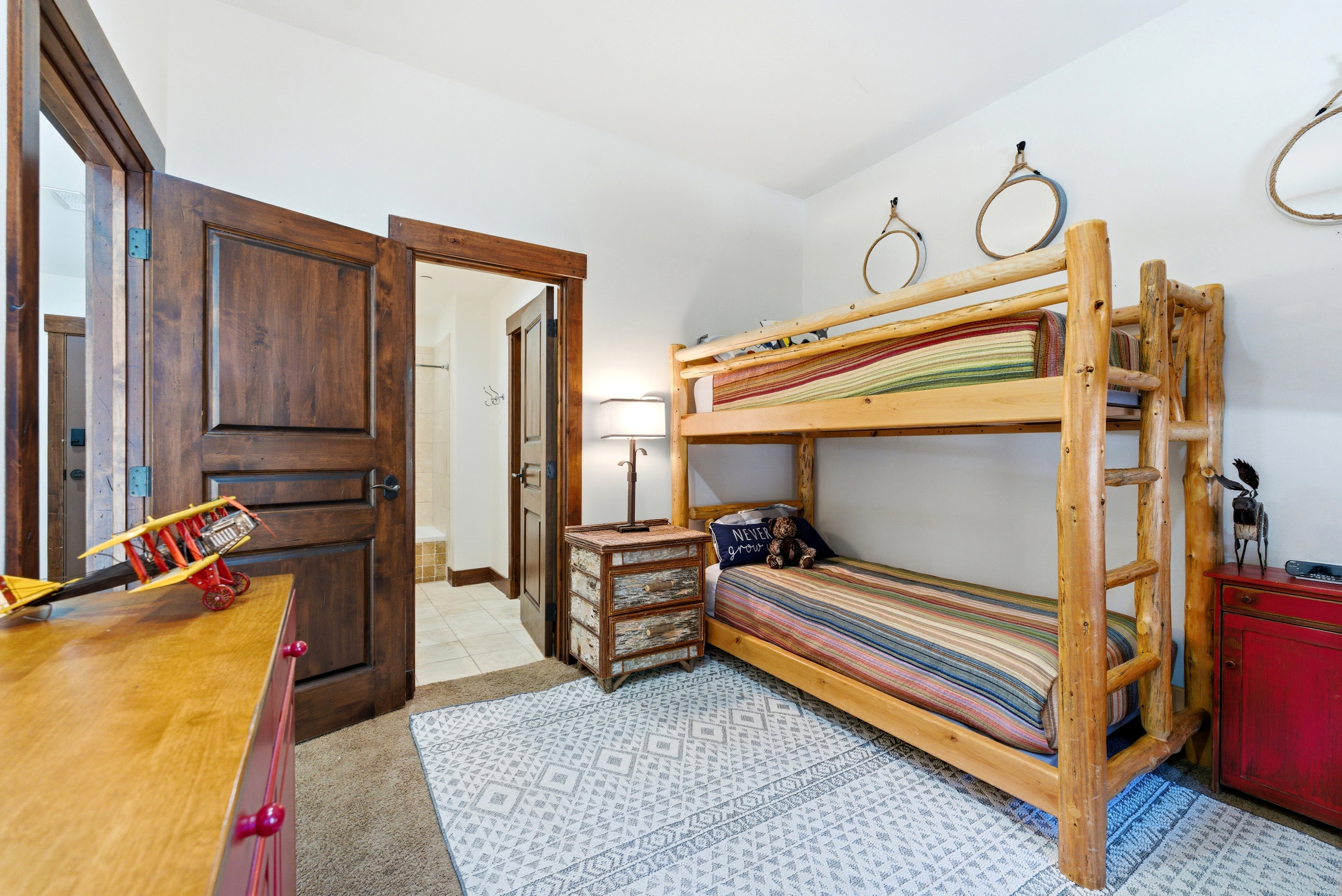 Room featuring a wood-finish bunk bed frame, a patterned area rug over carpeted flooring, and solid wood interior doors