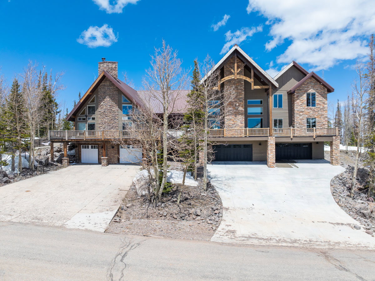 Stone and wood-sided architectural style featuring multiple gable roofs, extensive decking, and a prominent stone chimney