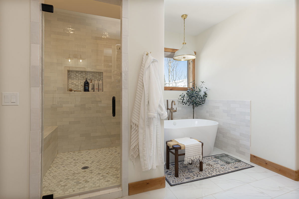 Freestanding soaking tub with brushed brass fixtures, complemented by a large walk-in shower featuring a built-in bench, glass enclosure, and mosaic tile flooring