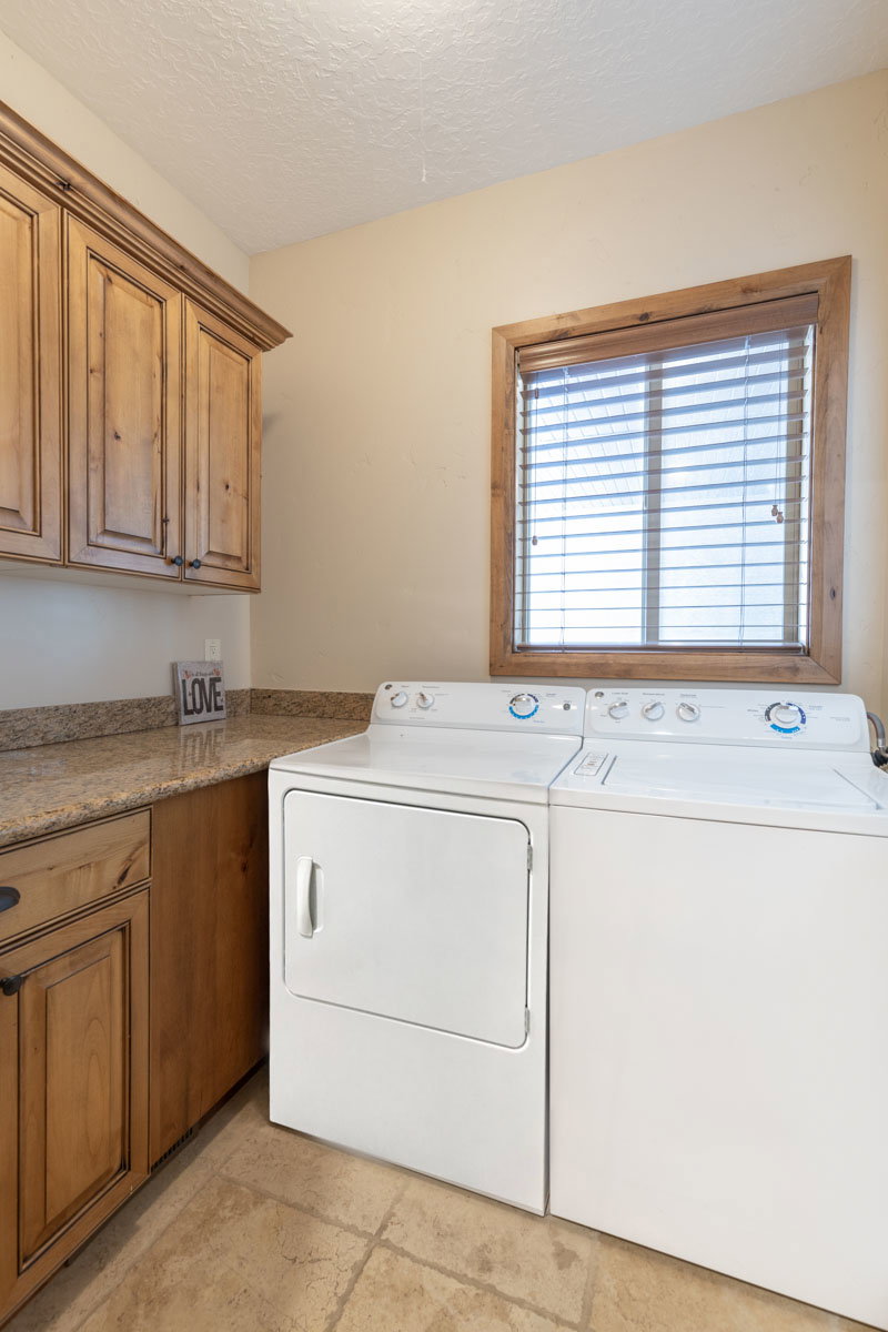 Laundry area featuring wood-finish cabinetry with dark hardware, a stone-finish countertop, and tiled flooring