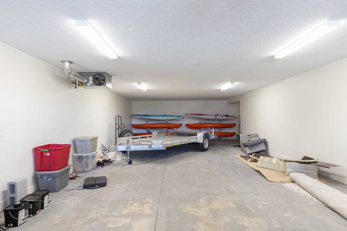 Spacious garage featuring a concrete floor, multiple ceiling-mounted fluorescent lights, white painted walls, and an exposed ventilation unit