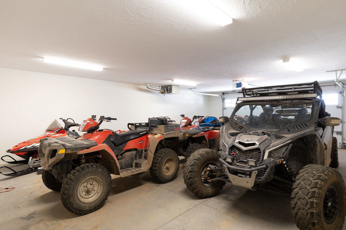 Spacious garage featuring a concrete floor, white walls, multiple fluorescent light fixtures, and a roll-up garage door with window inserts