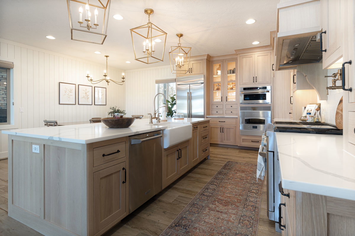 Spacious kitchen featuring an expansive center island with an integrated farmhouse sink, light wood-finish cabinetry, stainless steel appliances, and wood-finish flooring