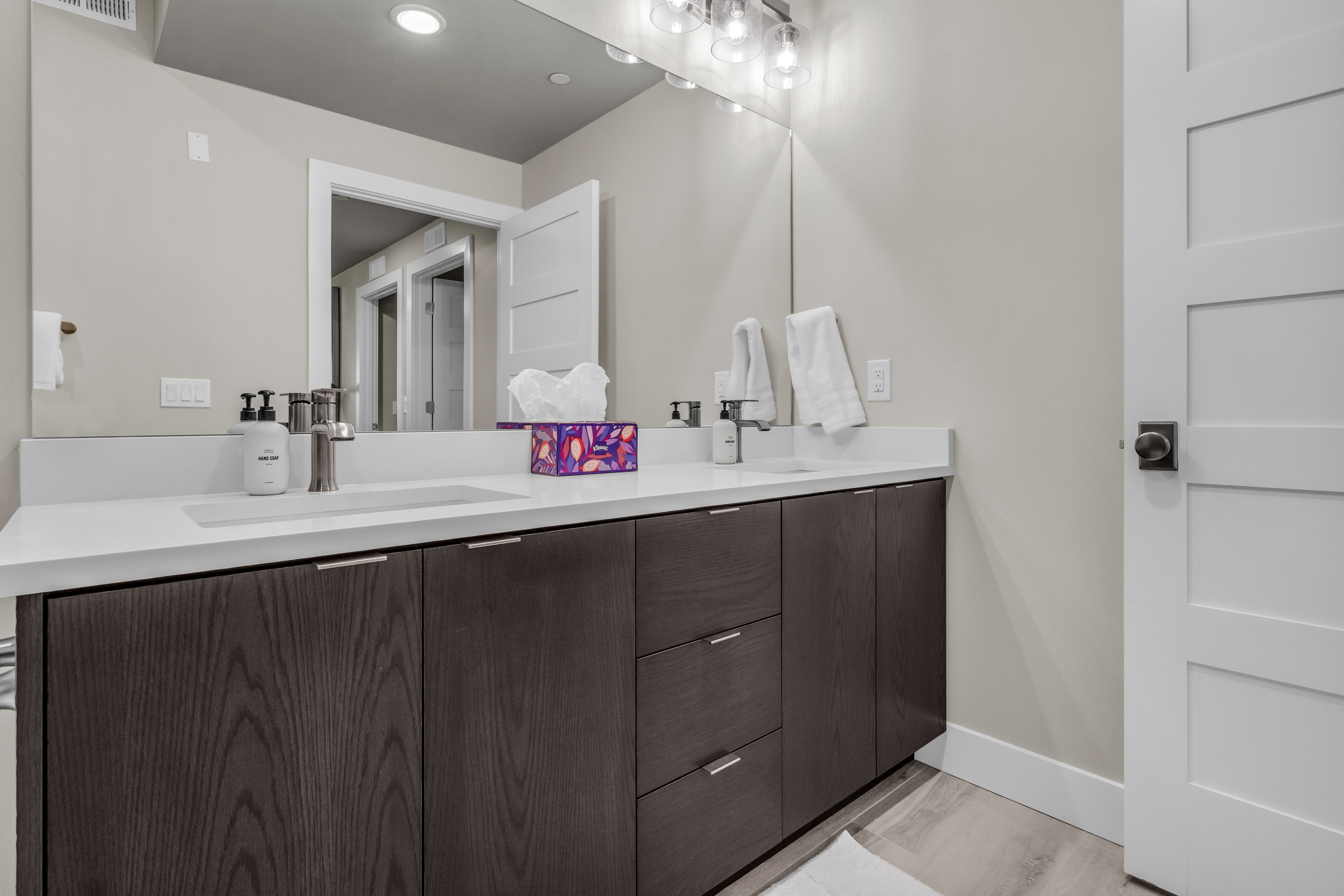 Double vanity with integrated sinks, white countertops, dark wood-finish cabinetry, and contemporary brushed nickel fixtures