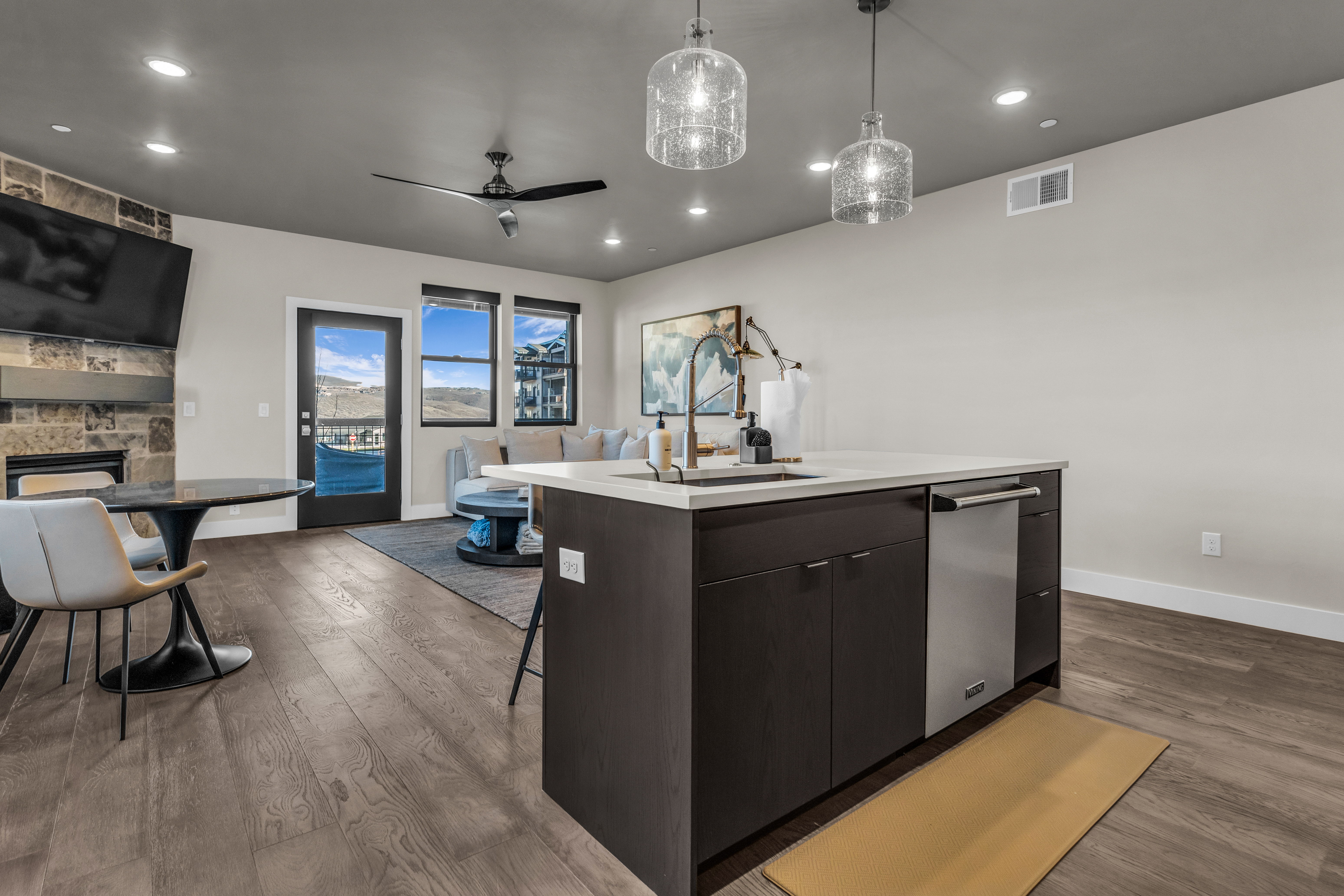 Open concept living area featuring wood-finish flooring, a kitchen island with sink and integrated dishwasher, recessed lighting, and large windows