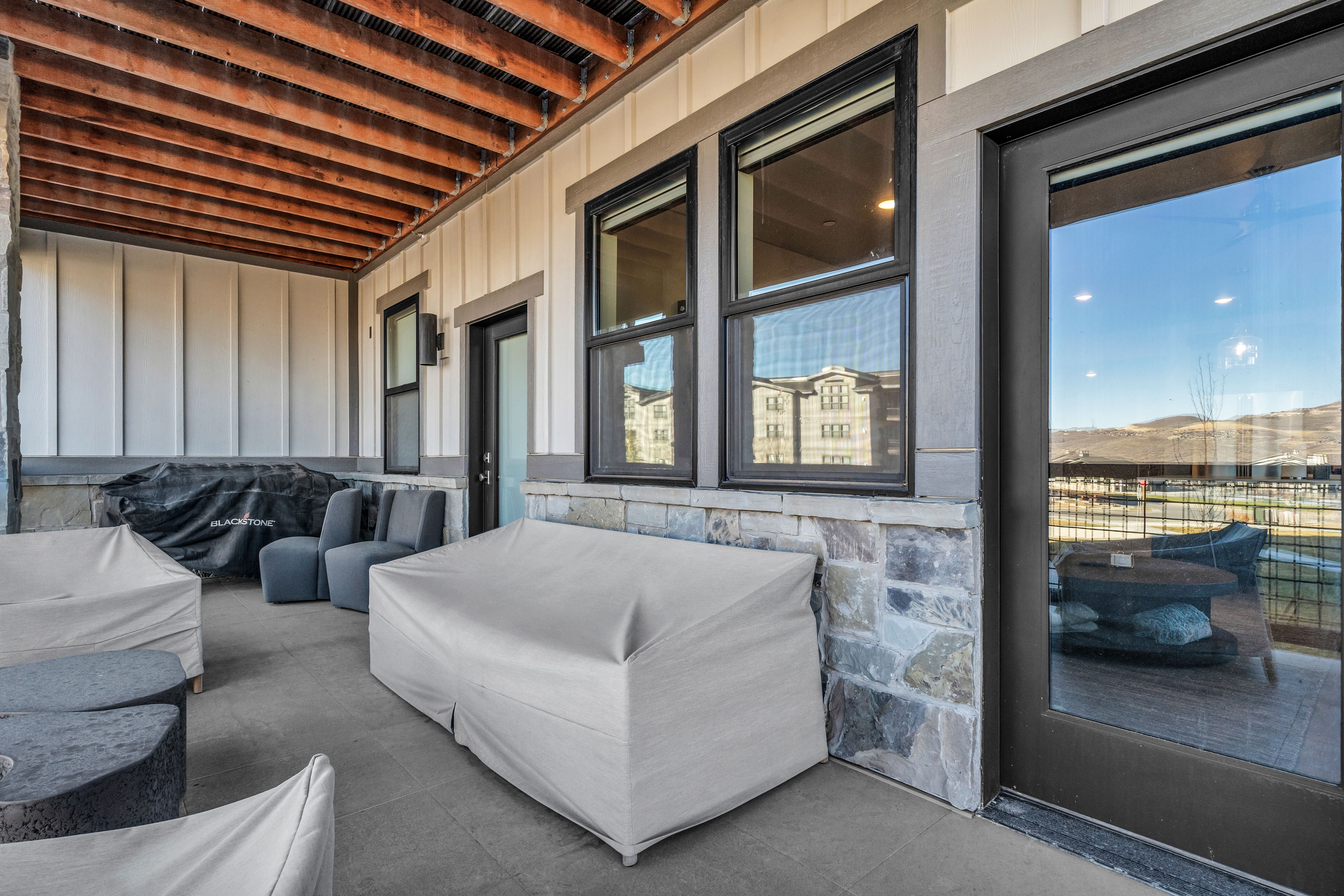 Covered patio featuring a wood-beam ceiling, stone accent wall, and durable concrete flooring