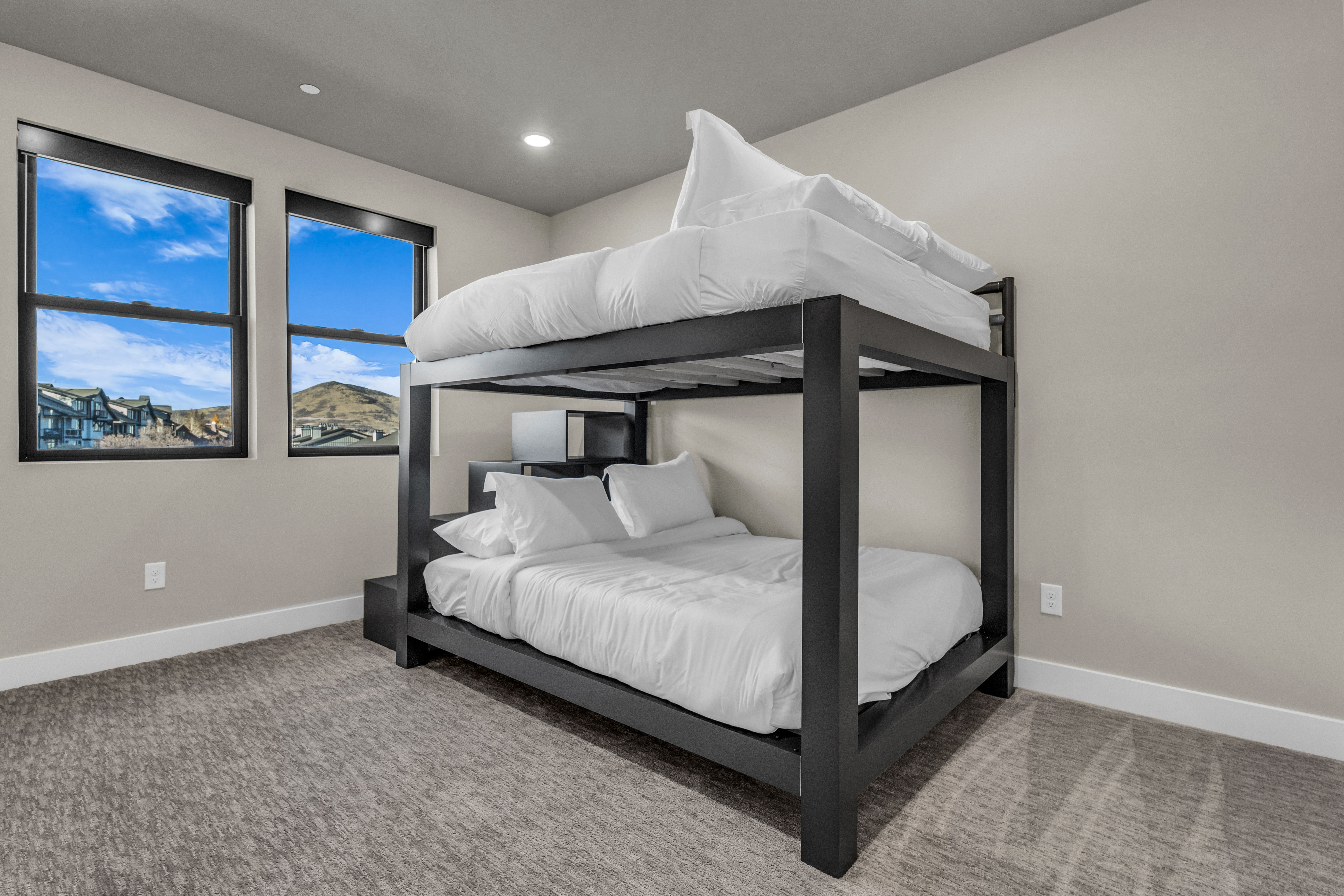 Bright bedroom featuring two windows with black trim, recessed lighting, and neutral-toned carpeting