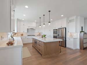 Kitchen featuring a large wood-finish island with a built-in microwave, white shaker-style cabinetry, stainless steel appliances, recessed lighting, and wood-finish flooring