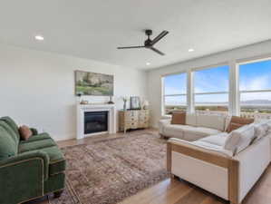 Spacious living area featuring large picture windows, wood-finish flooring, a contemporary ceiling fan, recessed lighting, and a modern fireplace with a white mantel
