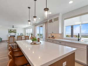 Spacious kitchen featuring a large island with pendant lighting, white perimeter cabinetry, light countertops, and an undermount sink with a black faucet