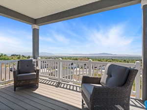 Covered outdoor balcony featuring composite decking, white railing, stucco columns, and a panoramic distant landscape