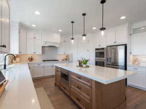 Spacious kitchen featuring an expansive center island with built-in microwave, white shaker cabinetry, stainless steel appliances, and wood-finish flooring
