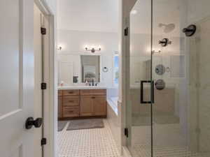 Modern bathroom featuring a glass-enclosed shower with dark bronze fixtures, a double vanity with wood cabinetry, a built-in bathtub, and mosaic tile flooring