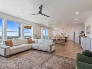 Open concept living space featuring a wall of windows, recessed lighting, wood-finish flooring, a modern ceiling fan, and a kitchen with white cabinetry