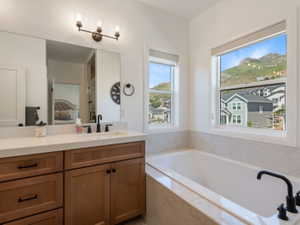 Bathroom featuring a built-in soaking tub with a matte black fixture, dual windows, and a wood-finish vanity with a light-toned countertop