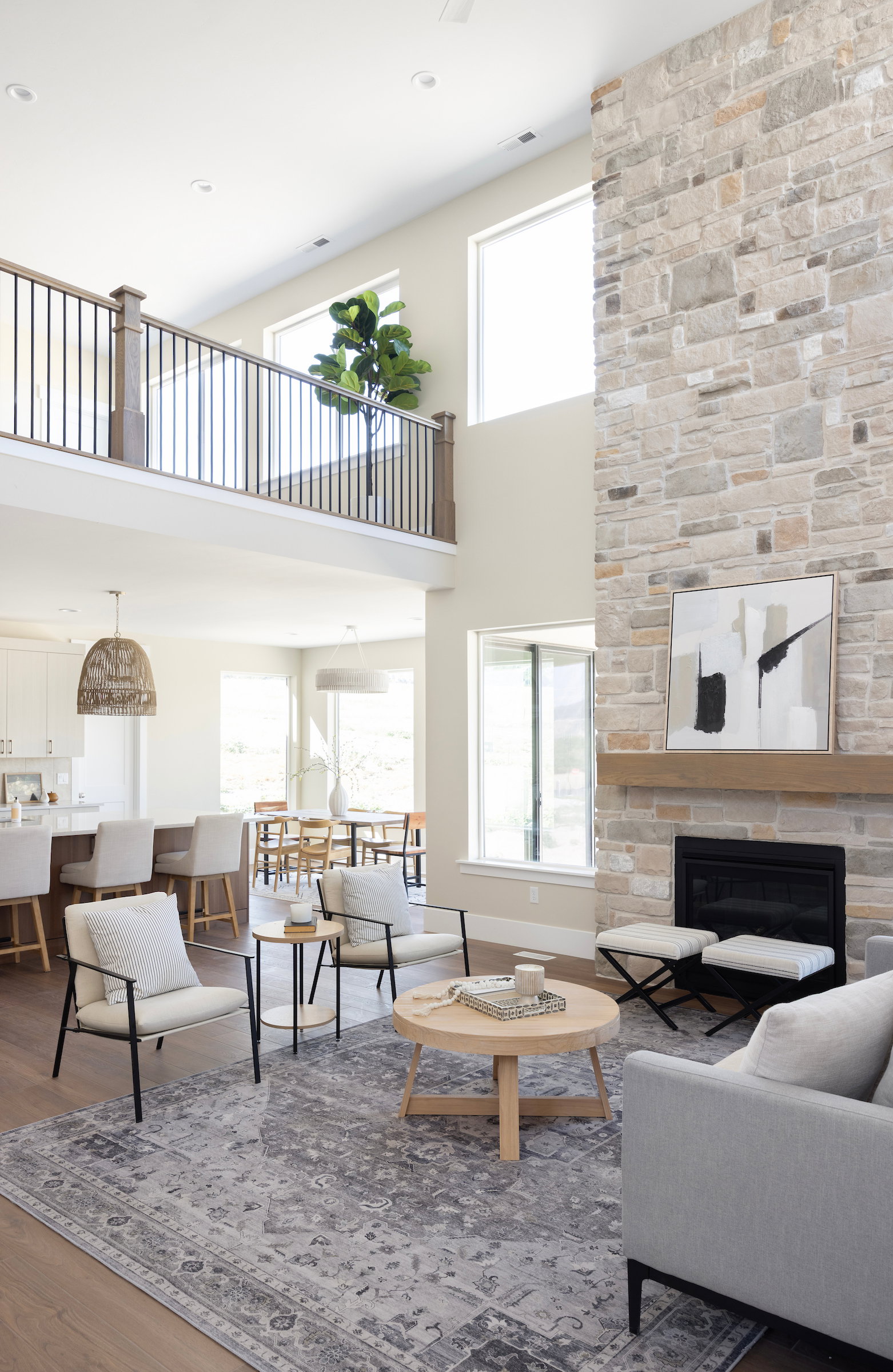 Two-story living area featuring a stone accent wall with an inset fireplace, a wood mantel, and large windows