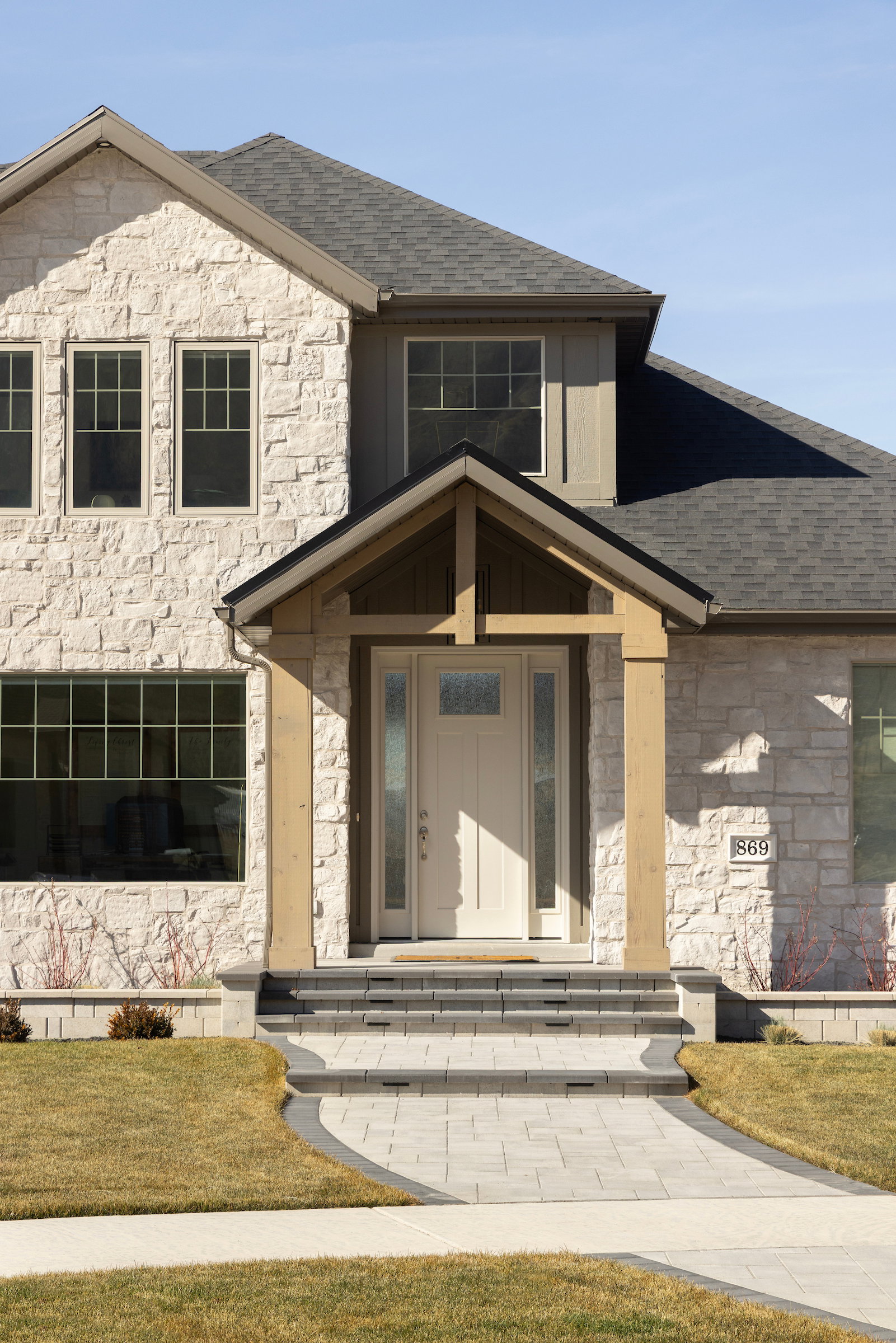Stone facade home featuring a prominent gabled entry with wood columns, a paneled front door with sidelights, and a paver walkway with steps