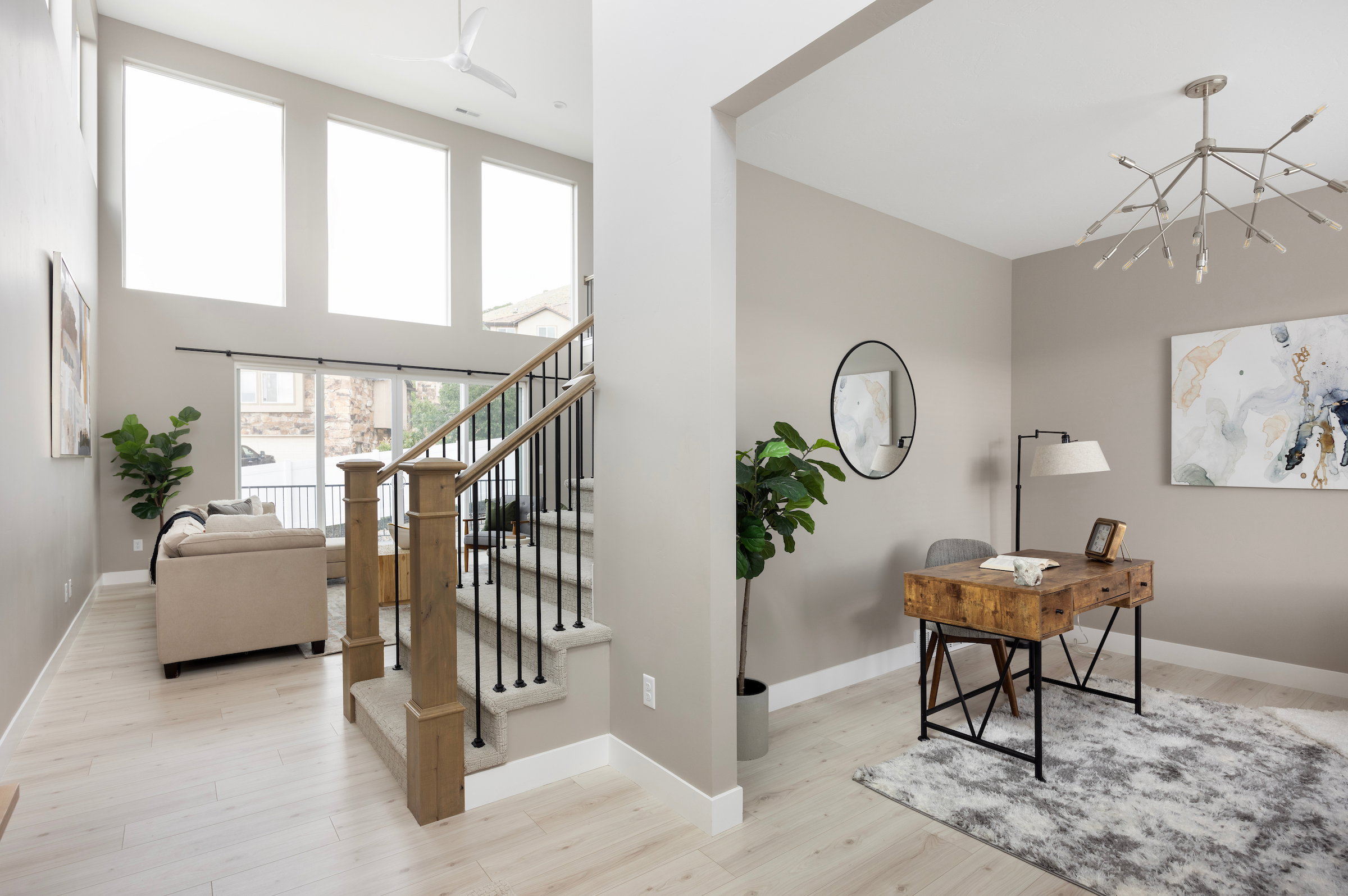 Two-story living area with high ceilings and a wall of three large windows, featuring a staircase with wood newel posts and black iron balusters