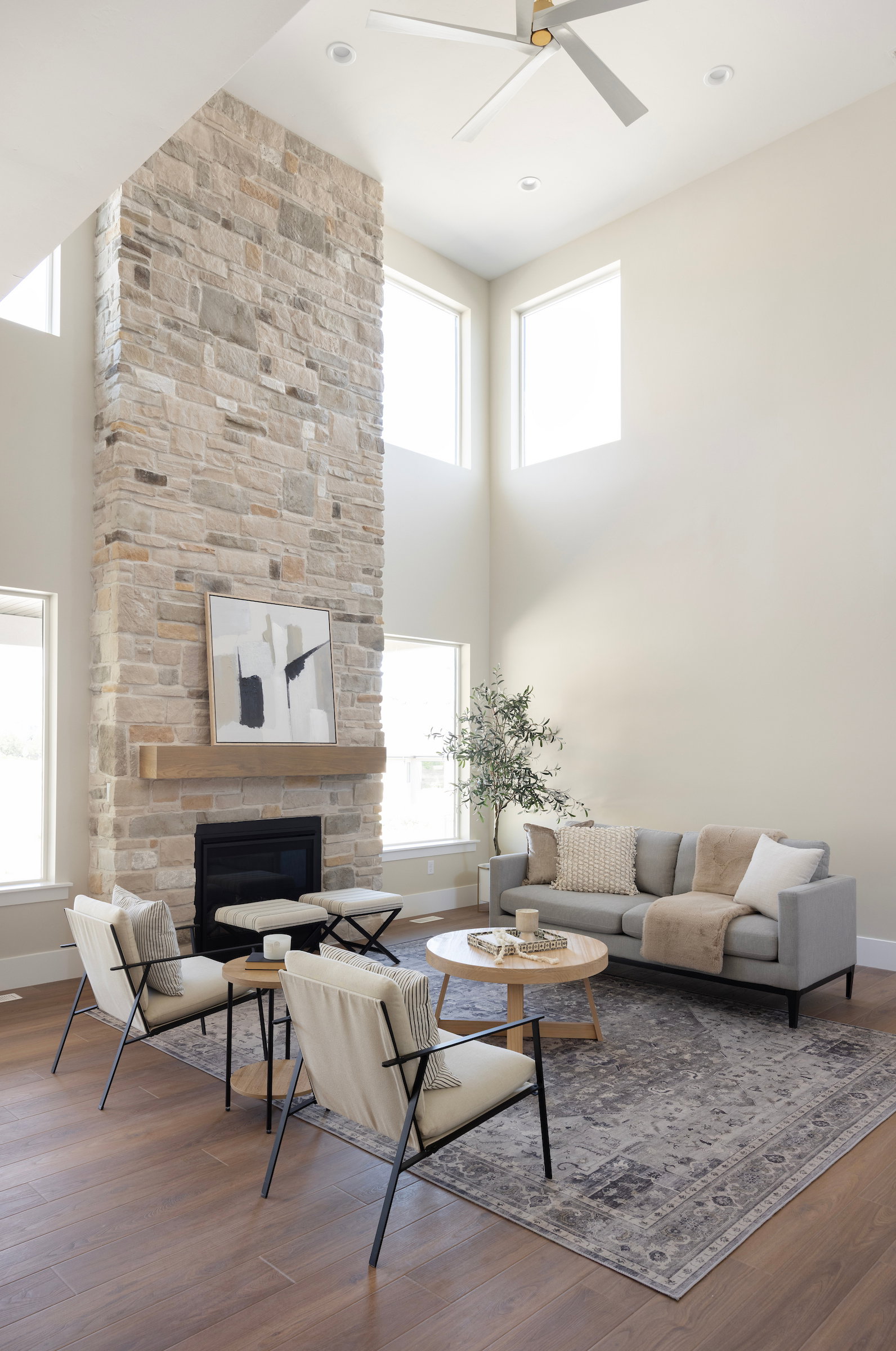 Two-story living area featuring a stone-clad fireplace with a wood mantel, wood-finish flooring, recessed lighting, and multiple windows