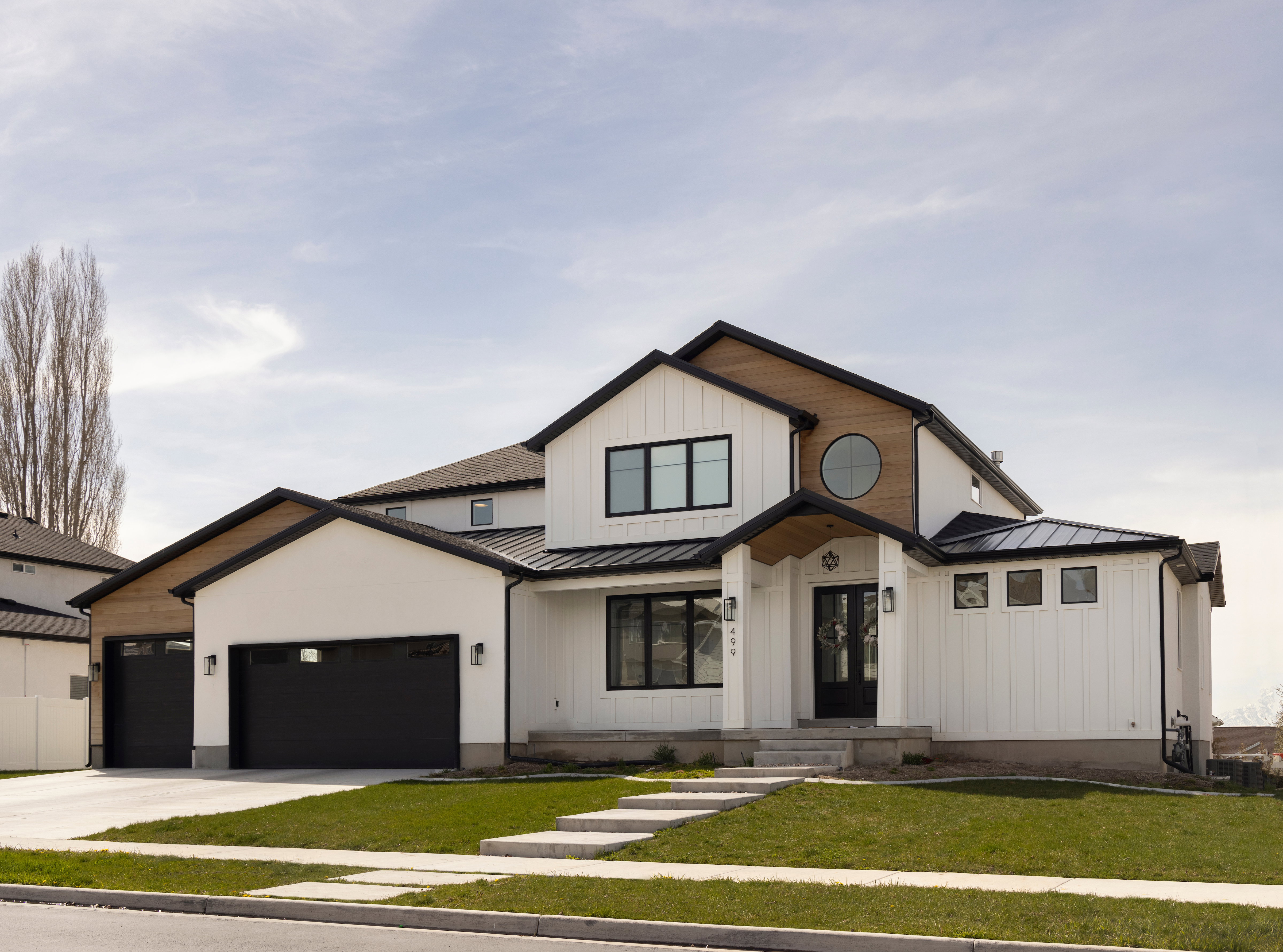 Modern farmhouse-inspired exterior featuring white board-and-batten siding, black-framed windows, and a prominent round window accent