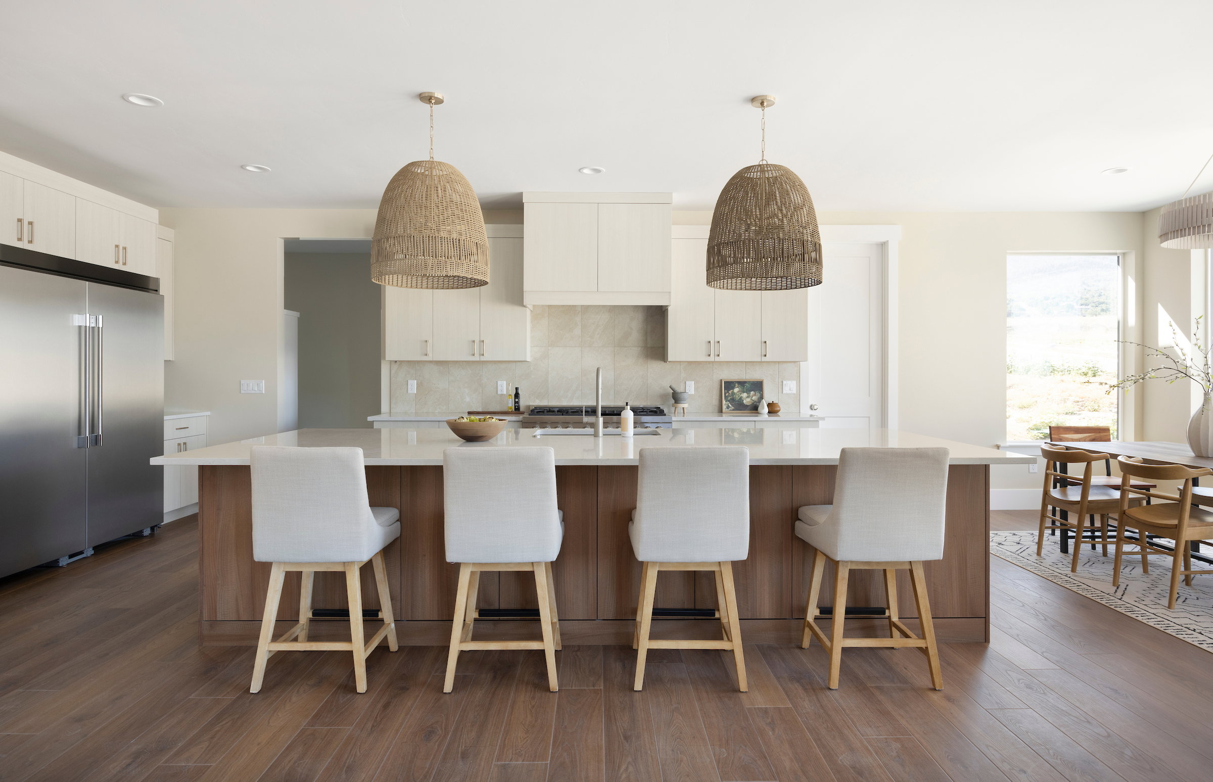 Contemporary kitchen featuring a spacious island with seating for four, wood-finish flooring, white upper cabinetry, stainless steel refrigerator, and pendant lighting