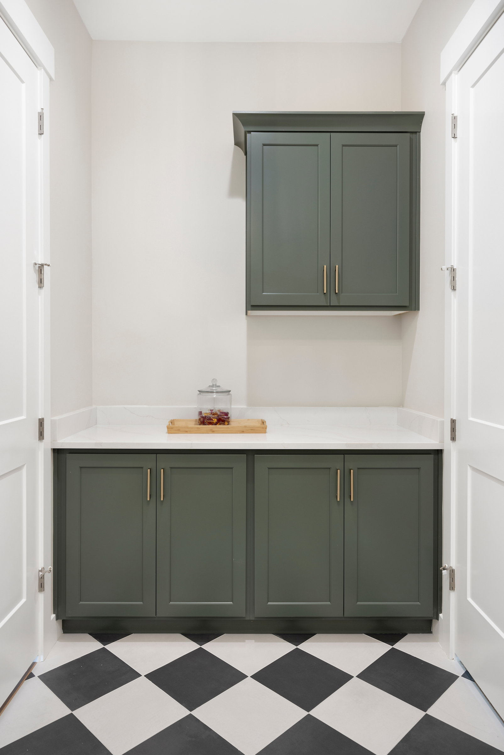 Built-in cabinetry in a muted green finish with brass hardware, featuring a white countertop
