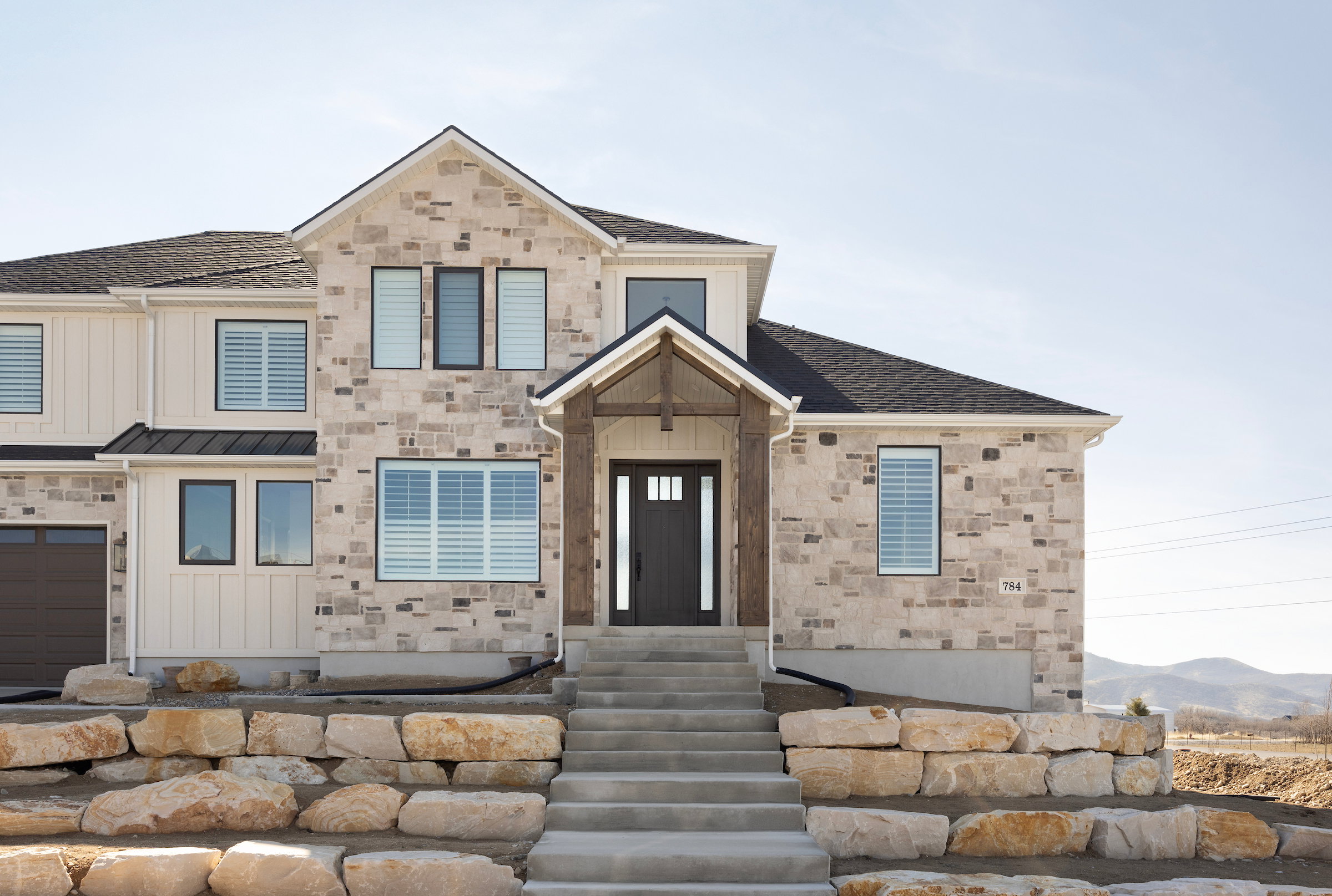 Stone and vertical plank siding exterior with a pitched roofline, prominent gabled entry, and dark-framed windows