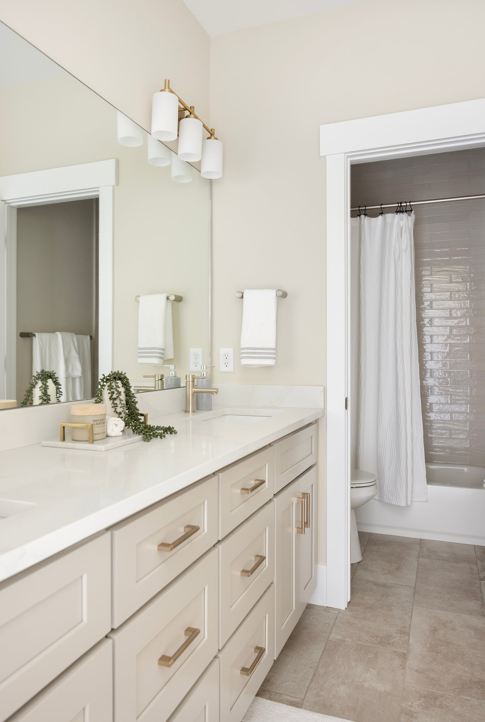 Double vanity featuring light-toned cabinetry with gold-toned hardware and white countertops