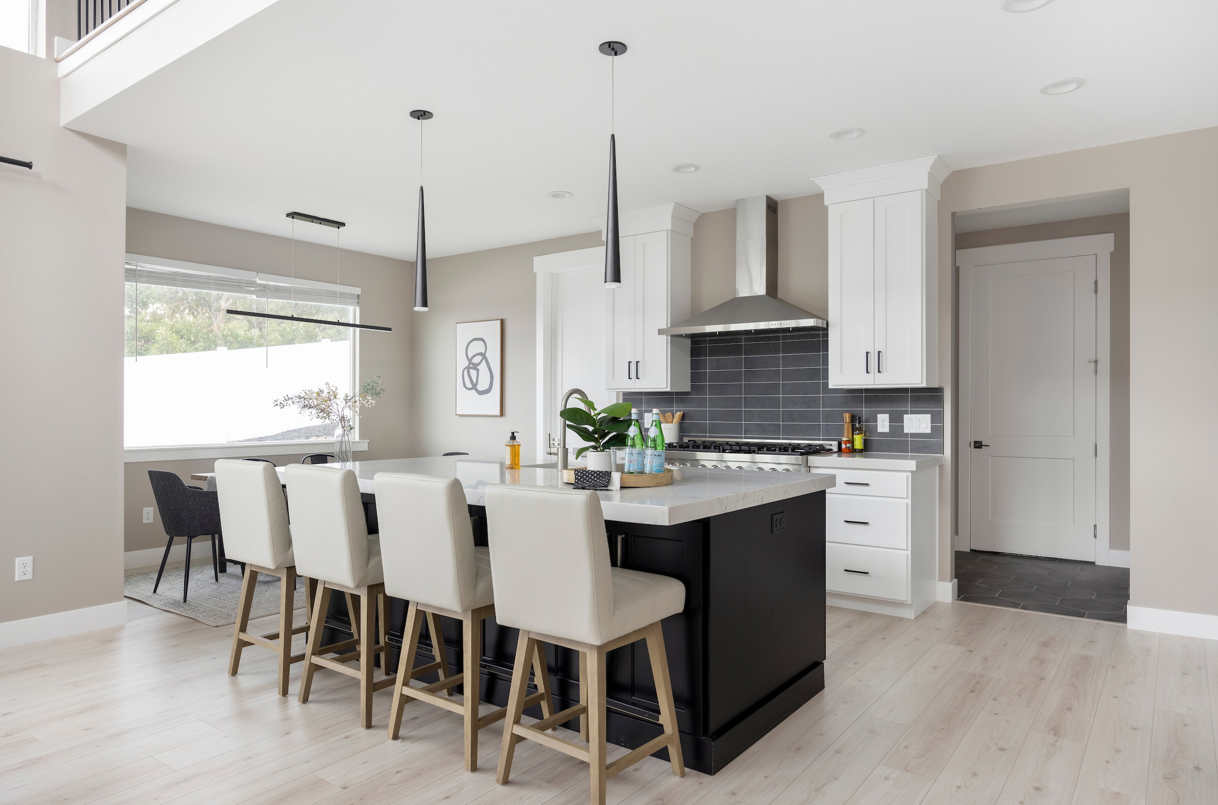Contemporary kitchen featuring a large island with white countertop, white upper and lower cabinetry, stainless steel range hood, and dark subway tile backsplash