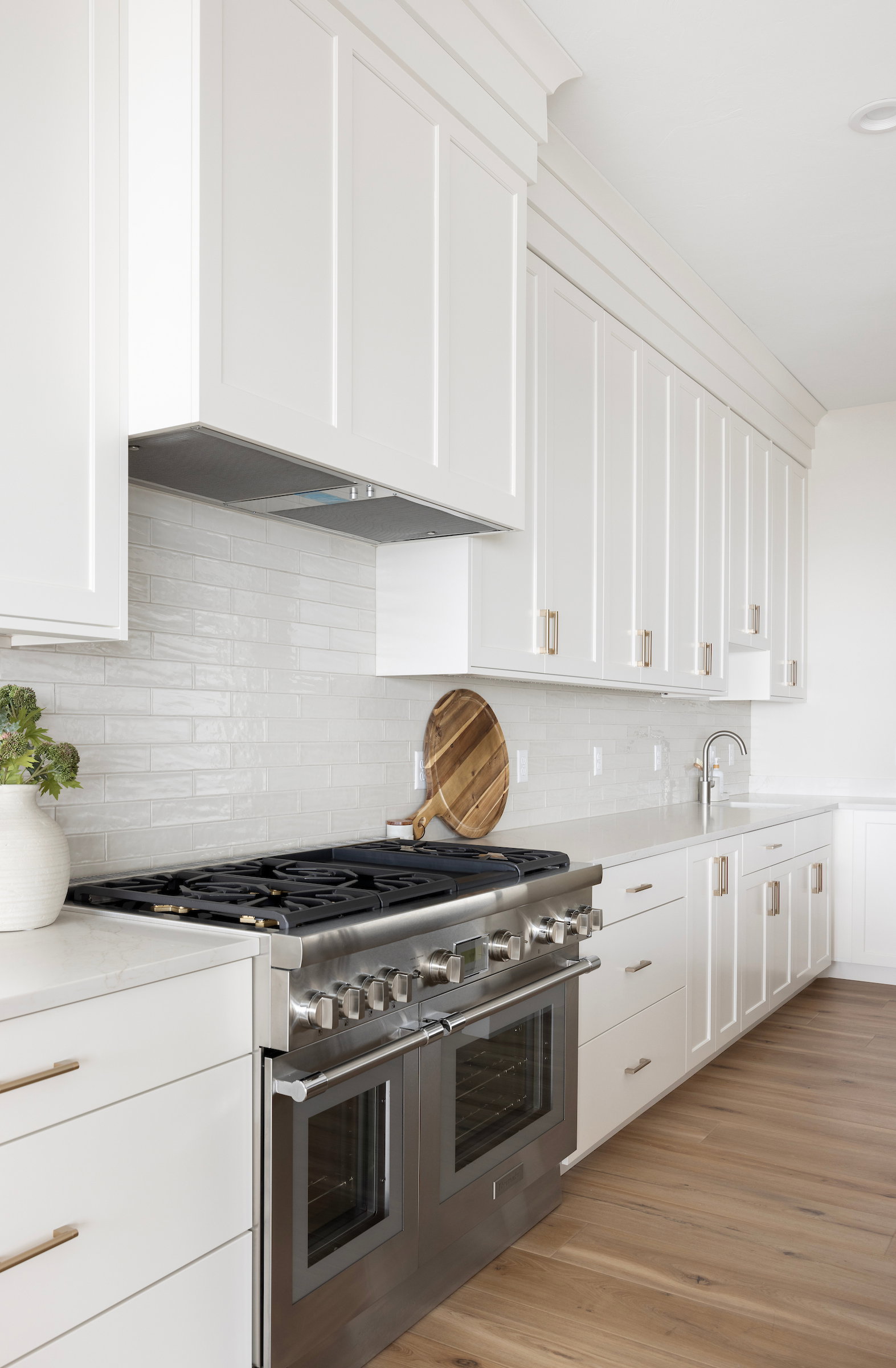Gourmet kitchen featuring a professional-grade stainless steel range with double ovens, white shaker cabinetry, light-toned countertops, a white subway tile backsplash, and wood-finish flooring