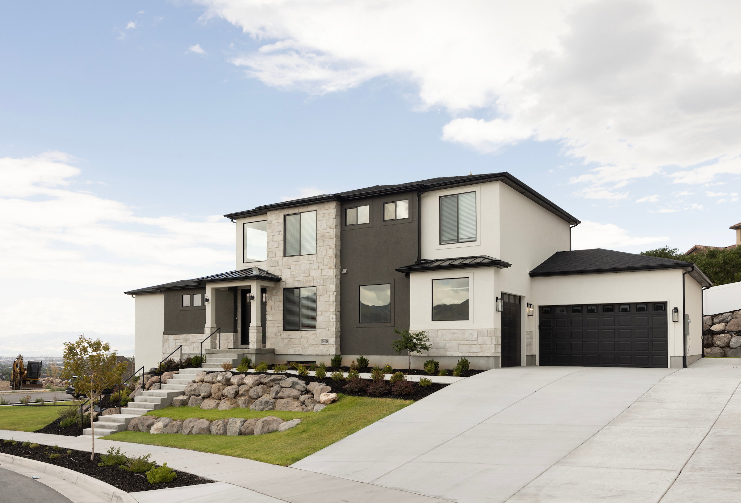Modern stucco and stone facade featuring a prominent two-car garage, concrete driveway, and tiered landscaping