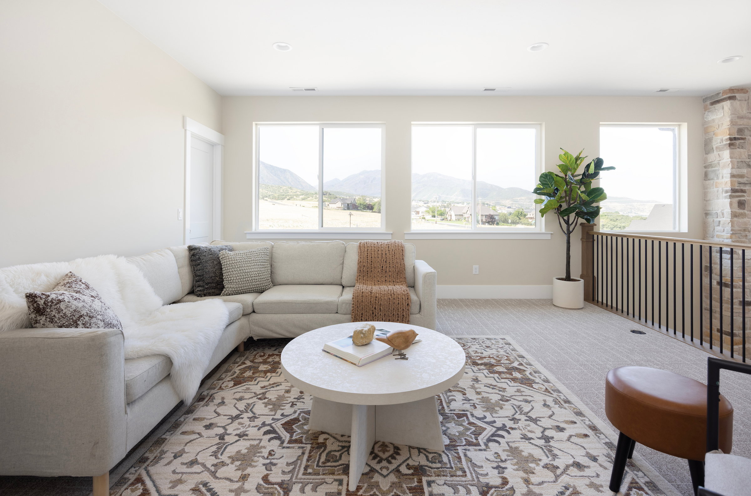 Upper-level bonus room featuring five large windows, light-colored carpeting, a stone-clad wall accent, and a black metal and wood railing