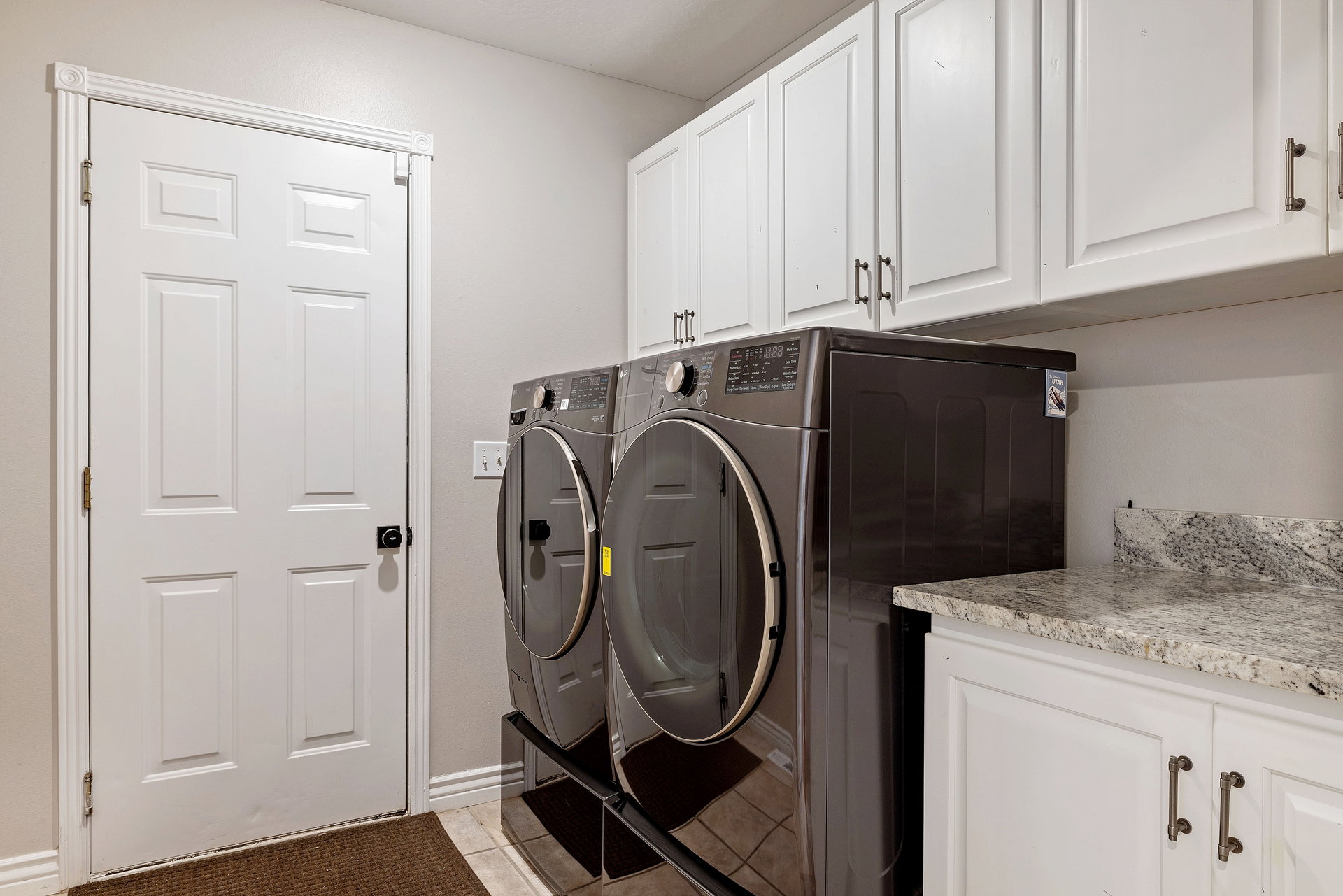 Functional laundry area featuring white shaker-style cabinetry, a light-toned stone-finish countertop, and matching lower cabinets