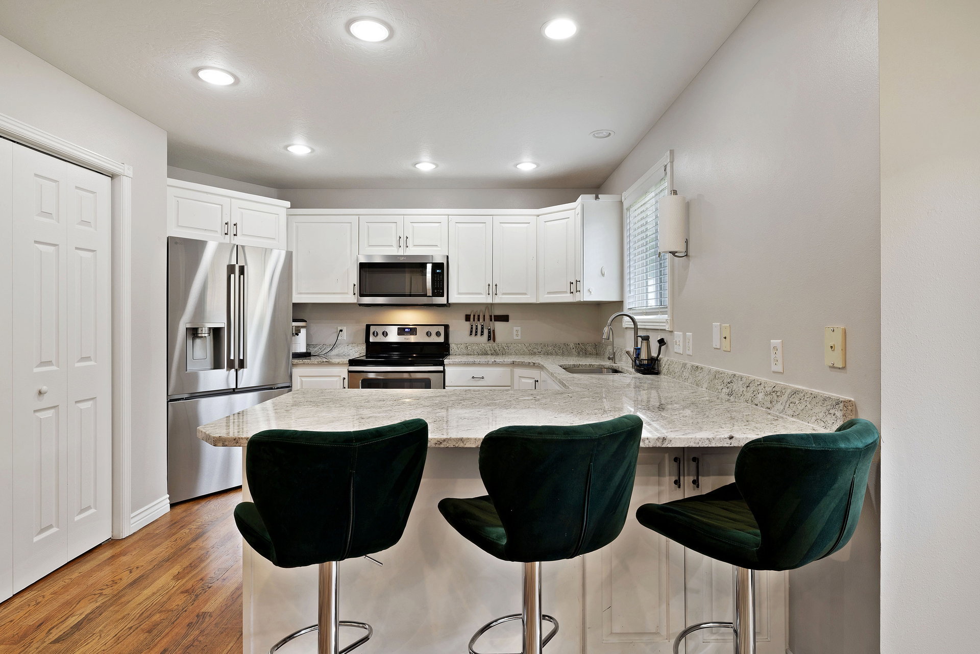 Kitchen featuring wood-finish flooring, white cabinetry, recessed lighting, and a peninsula with a light-toned countertop