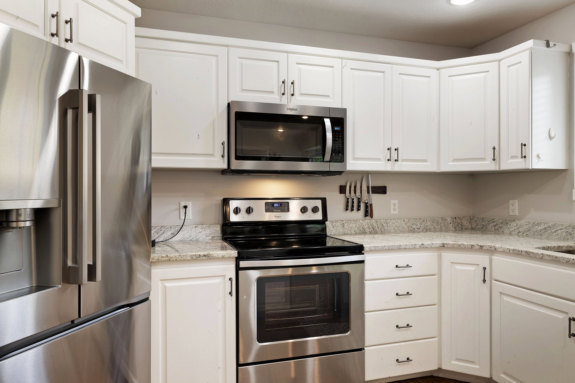 Modern kitchen featuring white shaker-style cabinetry, granite countertops, and stainless steel appliances including a side-by-side refrigerator, microwave, and range with oven