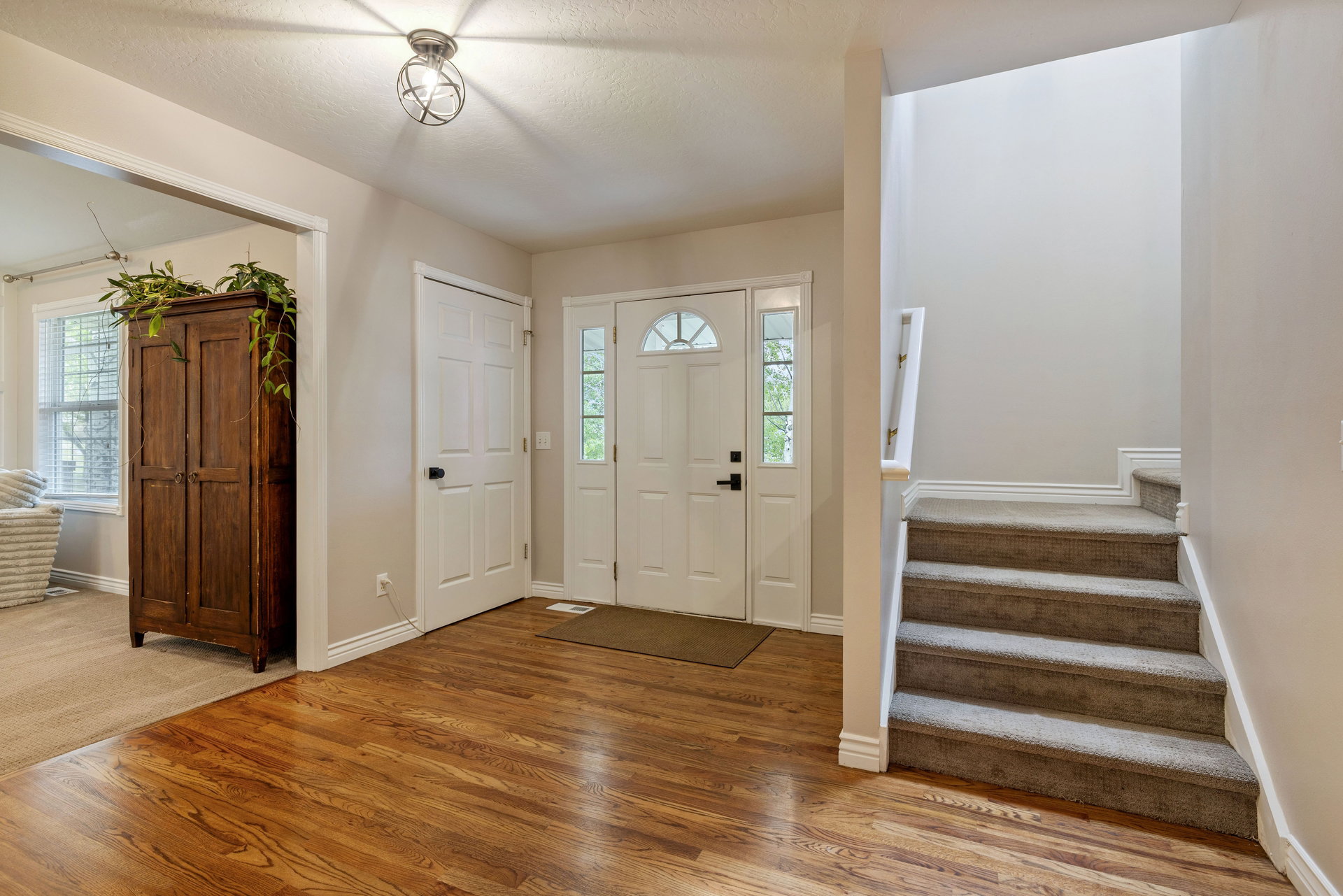 Entryway featuring wood-finish flooring, a white paneled front door with decorative glass inserts, and a carpeted staircase with white trim