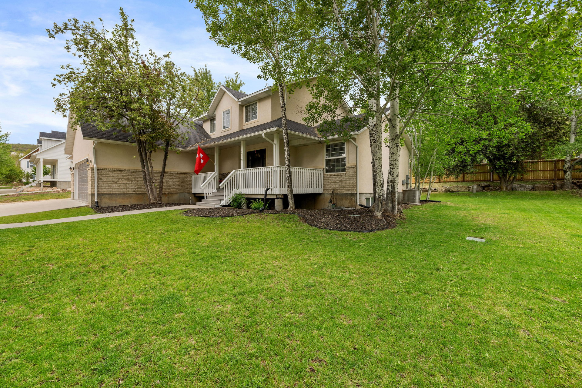 Stucco exterior with brick detailing, featuring a covered porch with white railings, a two-car garage, and mature trees