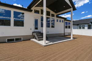 White stucco exterior featuring a covered patio, multiple windows, and a paved outdoor landing with steps