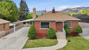Brick exterior residence featuring a front entry with concrete steps and white railings, a covered carport, and a prominent chimney