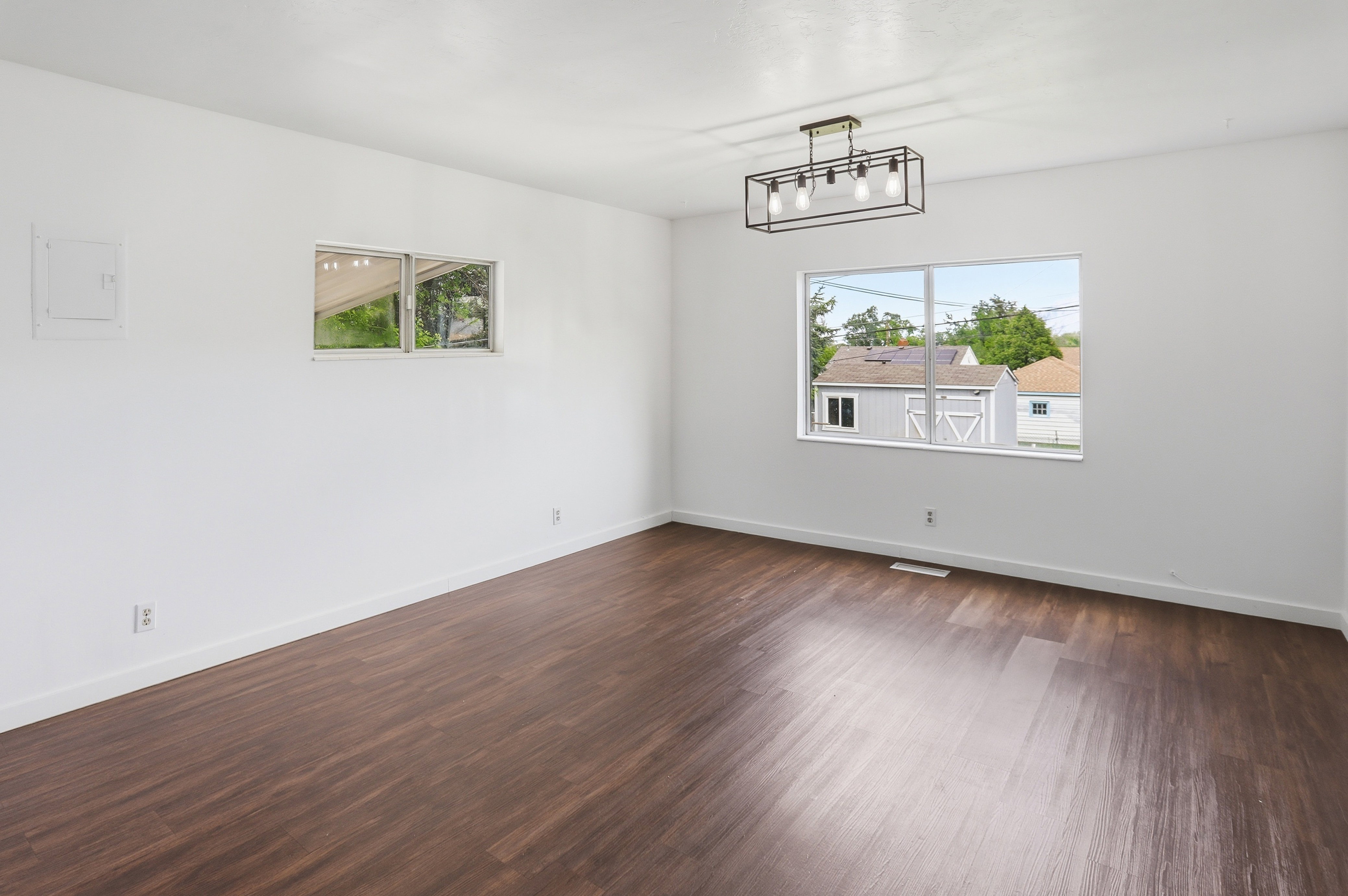 Spacious room featuring dark wood-finish flooring, crisp white walls, and a contemporary linear chandelier with exposed bulbs