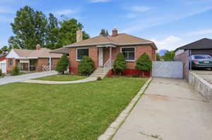 Brick exterior featuring a front lawn, paved driveway, and established landscaping