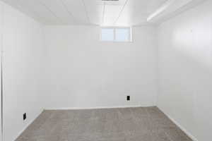 Finished room featuring neutral carpeting, white paneling walls, a drop ceiling, and a high window