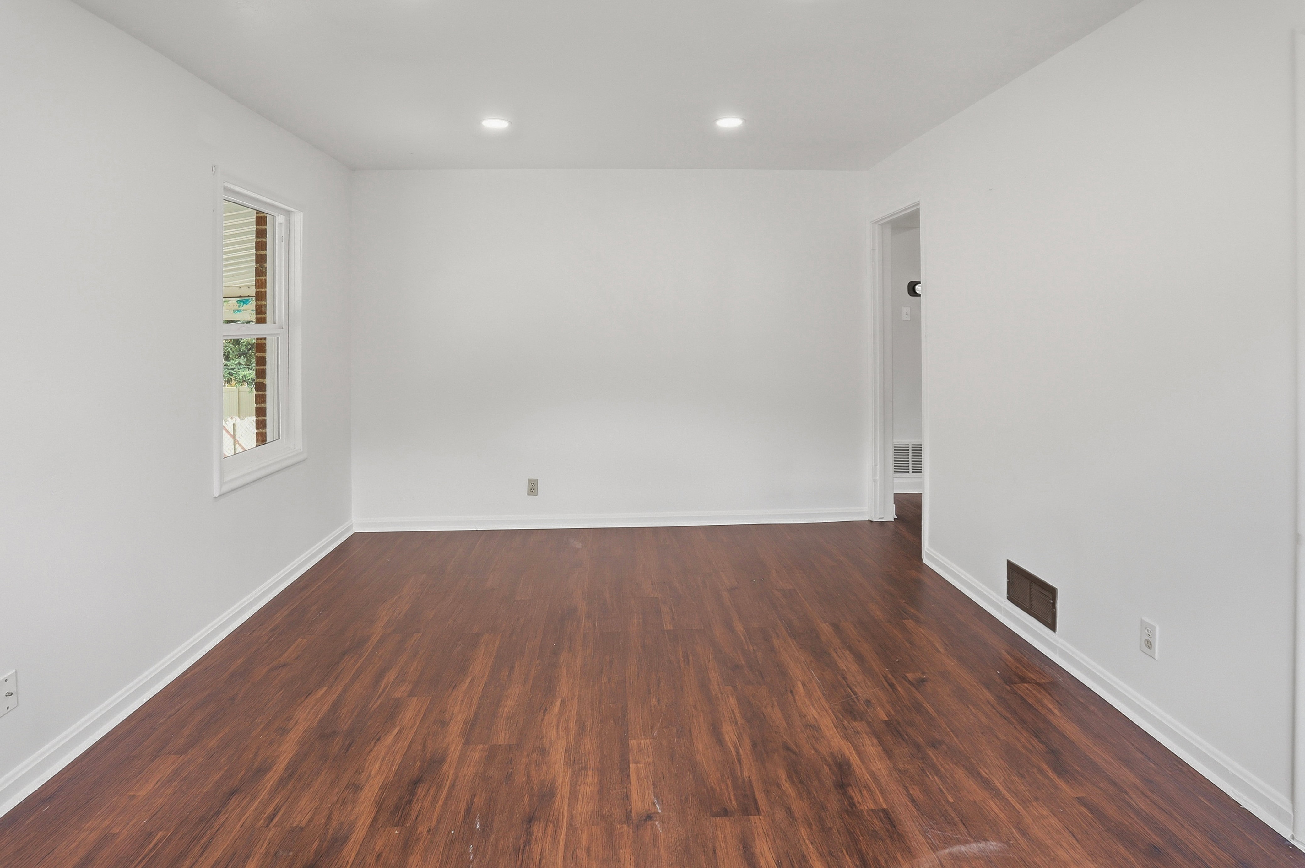 Spacious room featuring rich wood-finish flooring, crisp white walls, and recessed lighting