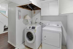 Dedicated laundry area featuring a washer and dryer, white cabinetry, and wood-finish flooring extending into the adjacent space