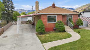 Brick exterior with a stone chimney, covered carport, concrete driveway, and a front walkway leading to the entry